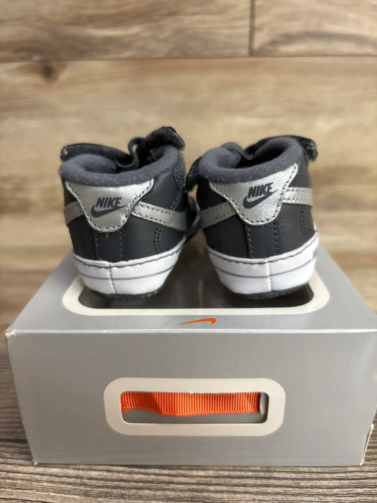 Gray and silver Nike toddler sneakers on a shoebox, wooden background
