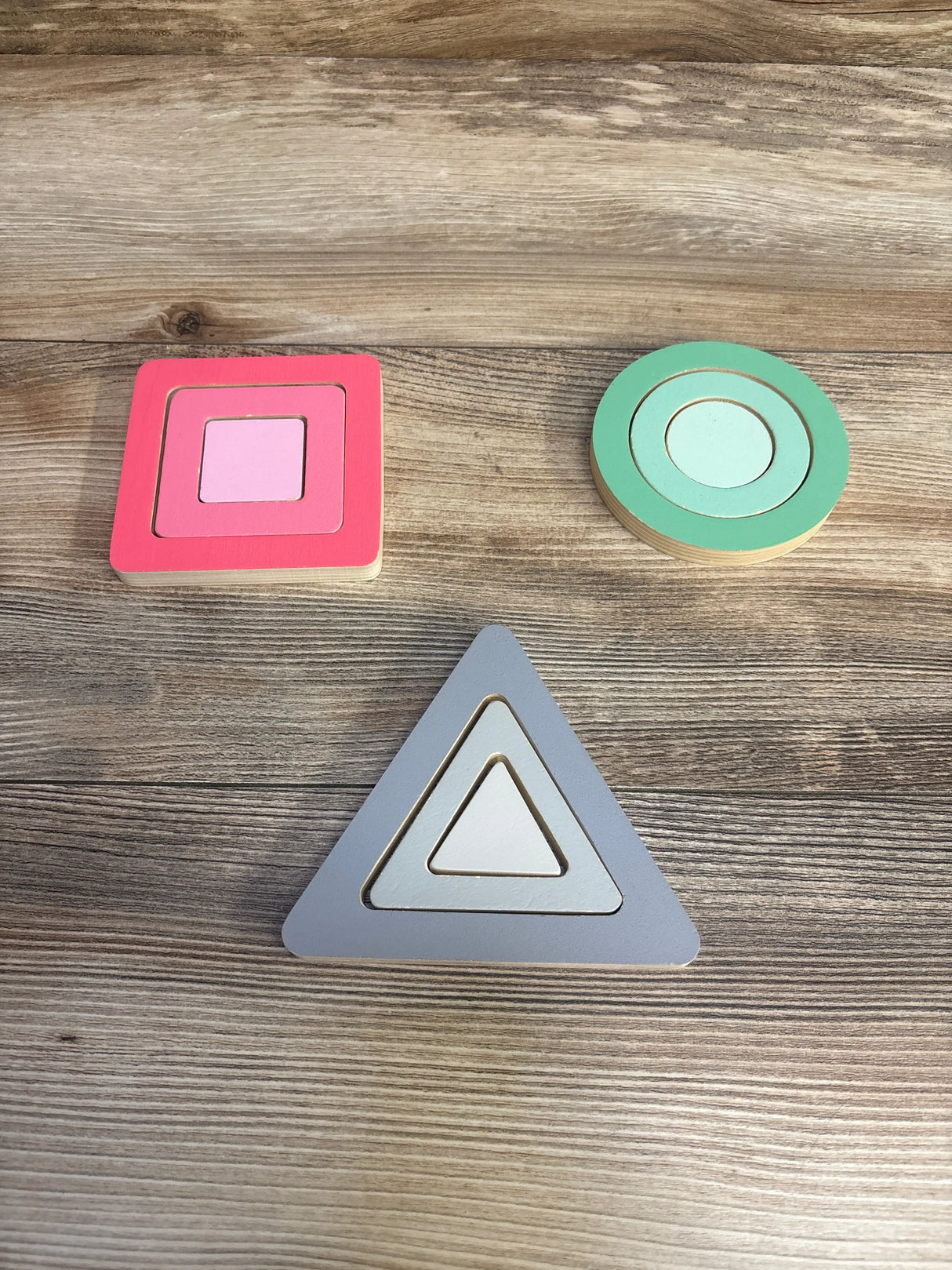 Top-down view of KiwiCo Panda Crate puzzle with three nested wooden shapes: pink square, mint circle, gray triangle on wood