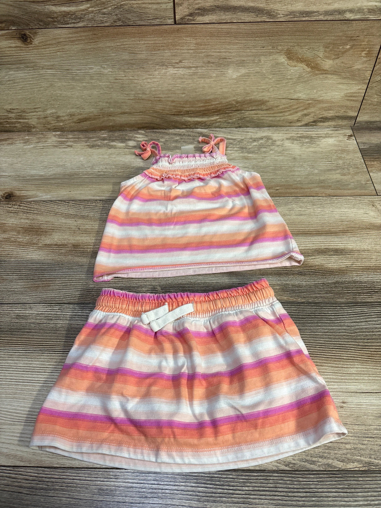 Flat lay of toddler striped tank top and skort showing peach, pink and white stripes on wood background