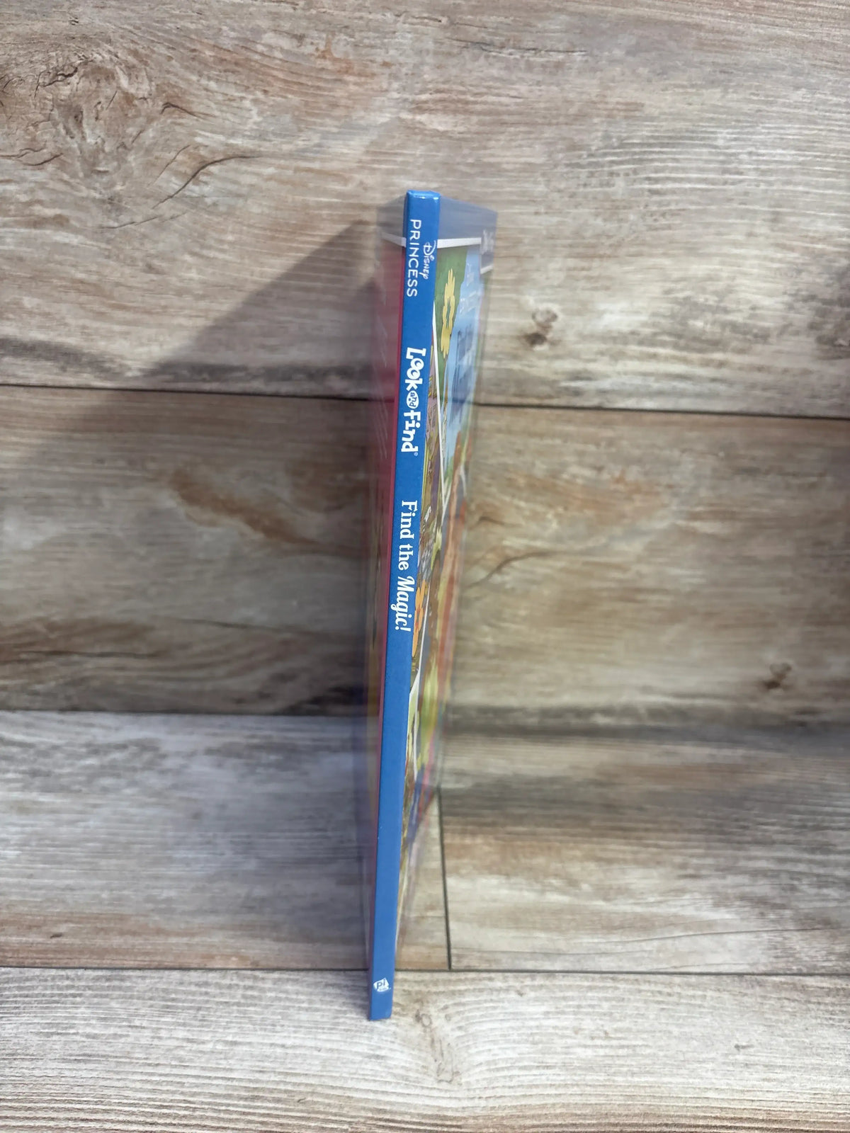 Spine view of Disney Princess Find the Magic Look and Find hardcover activity book showing blue binding on a wood surface