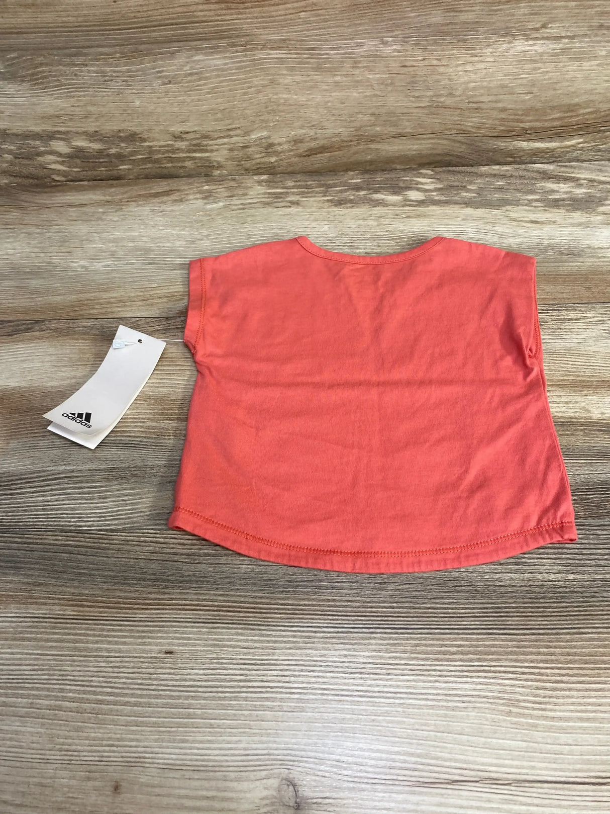 Back view of red Adidas baby t-shirt size 3-6 months showing short sleeves, curved hem, and Adidas tag on wood background