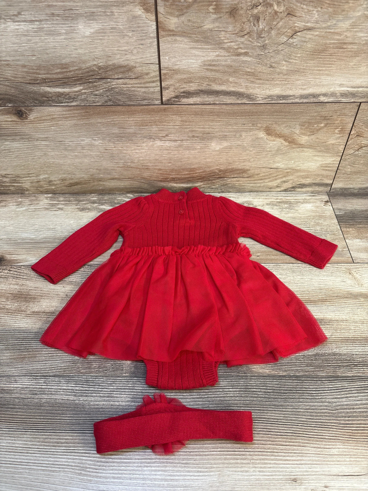 Red baby dress with tulle skirt, long sleeves, and matching headband on wood floor