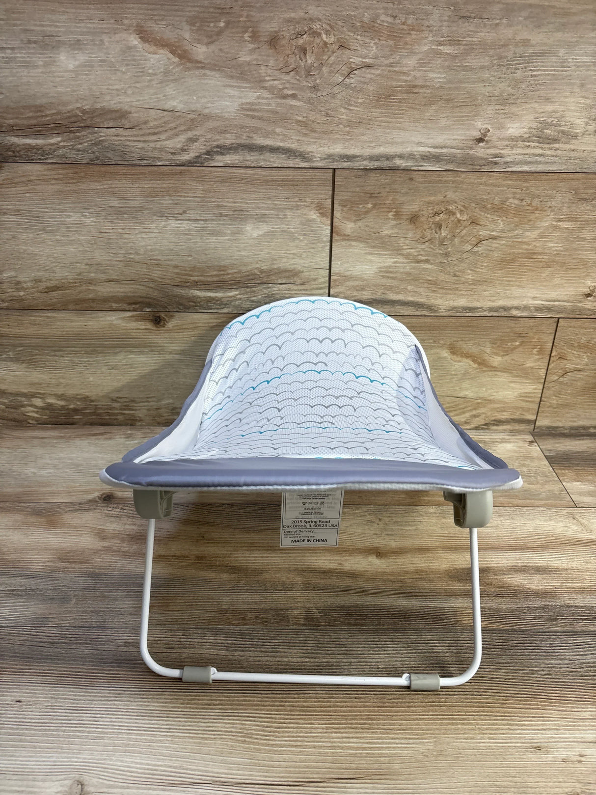 Front view of Summer Deluxe baby bather in grey with mesh scallop seat and white foldable frame on wood background