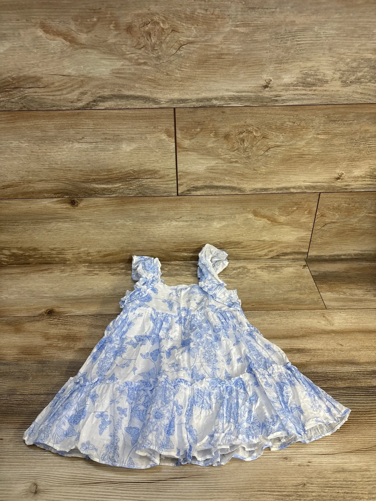 Front view of Bonnie Baby flutter sleeved toile clip dot dress showcasing blue floral print and ruffle seam on wood floor