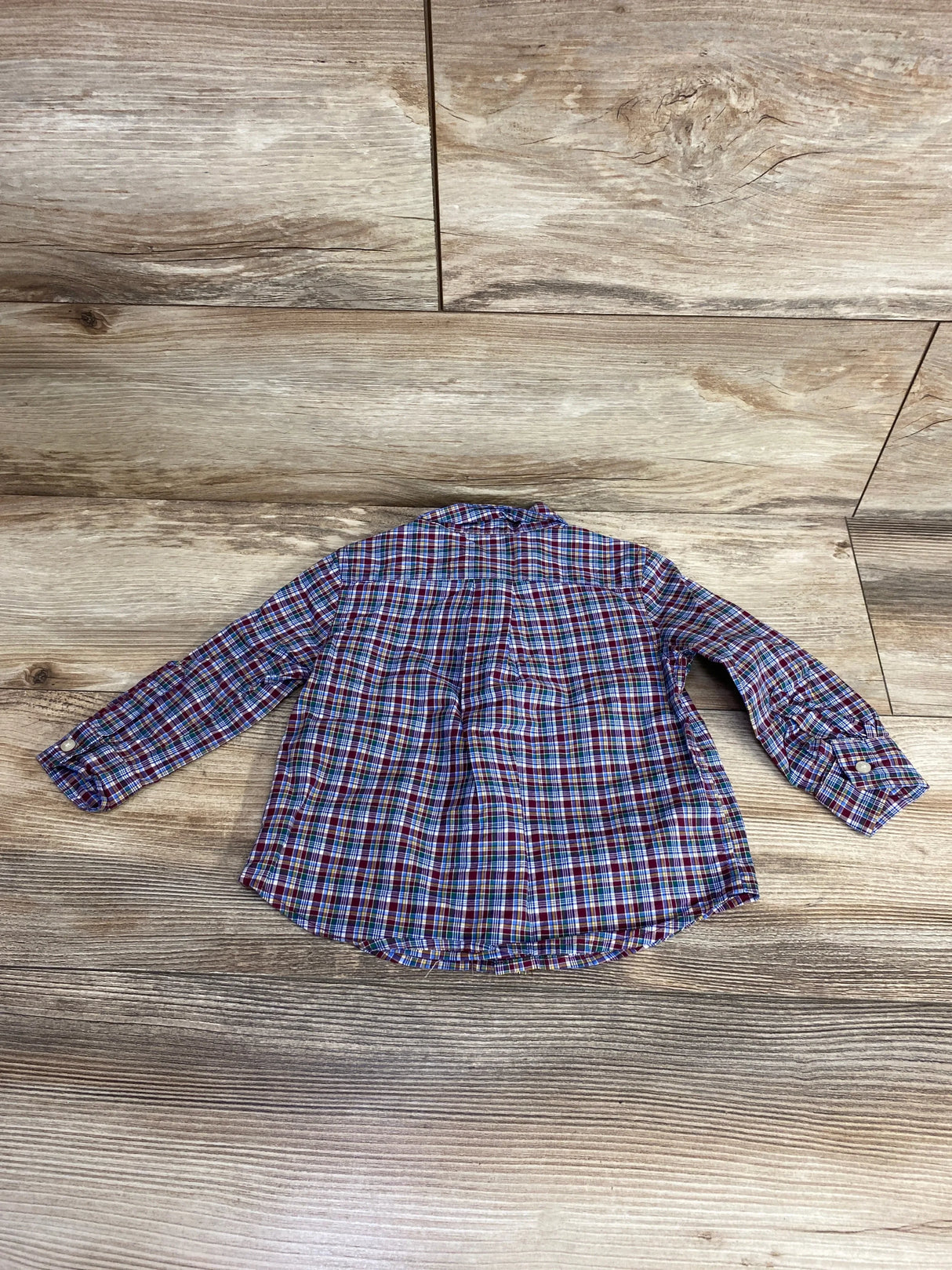 Plaid long sleeve button-up shirt for kids displayed flat on wooden background