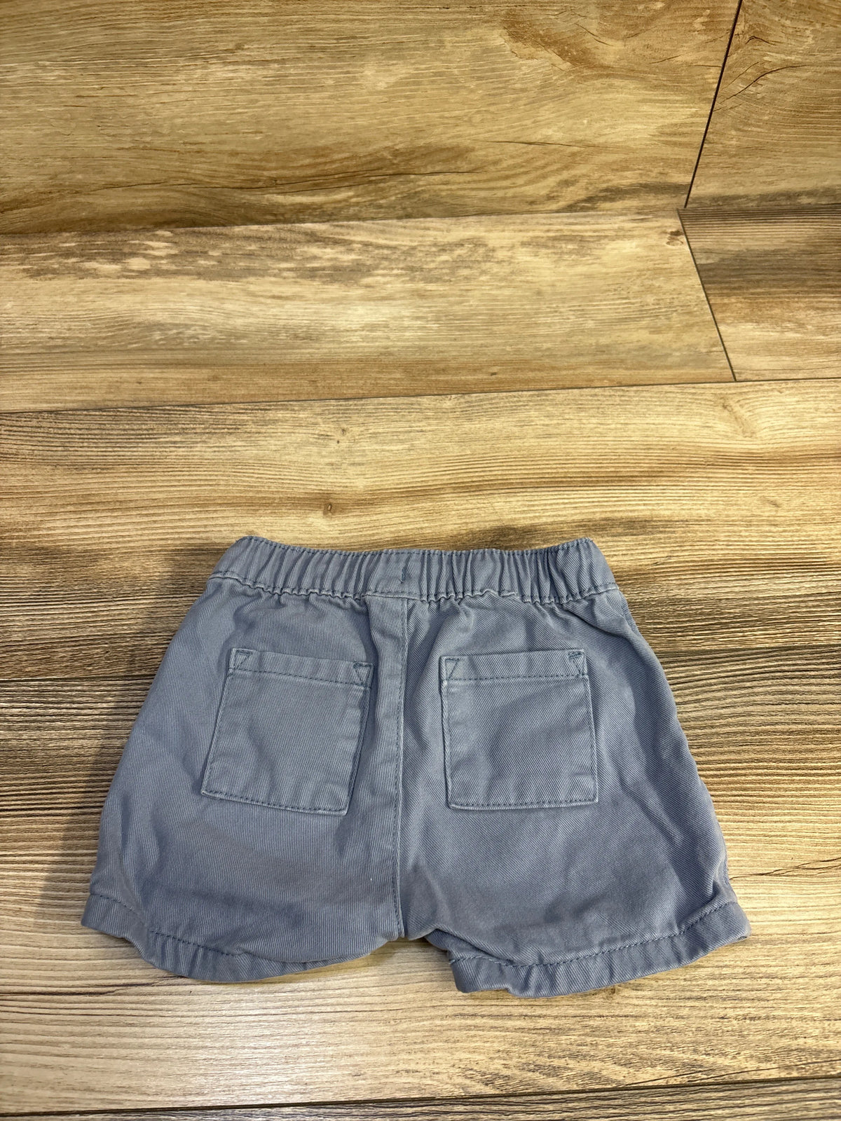 Back view of blue Old Navy baby drawstring shorts showing elastic waistband and two back patch pockets on wooden floor