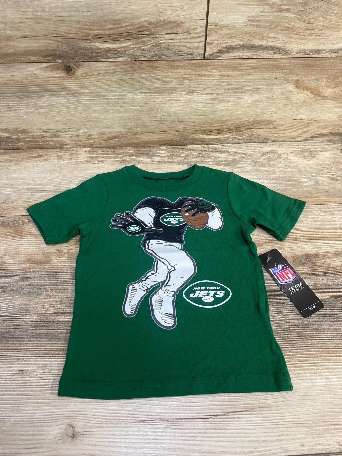 Front view of green New York Jets toddler T-shirt size 3T showing stiff-arm player graphic and NFL hang tag on wood floor