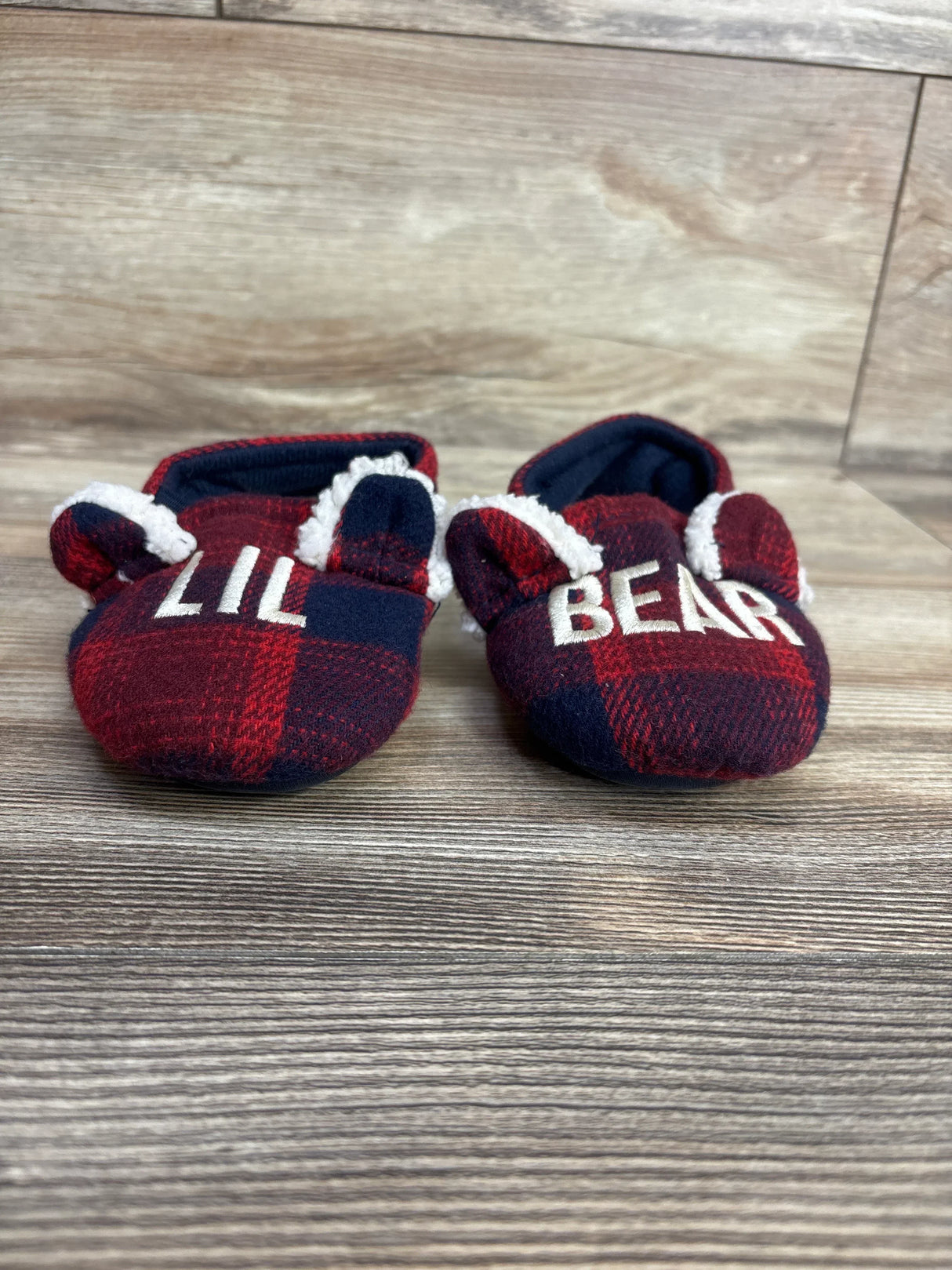 Plaid baby booties with bear ears and 'LIL BEAR' text on wooden floor