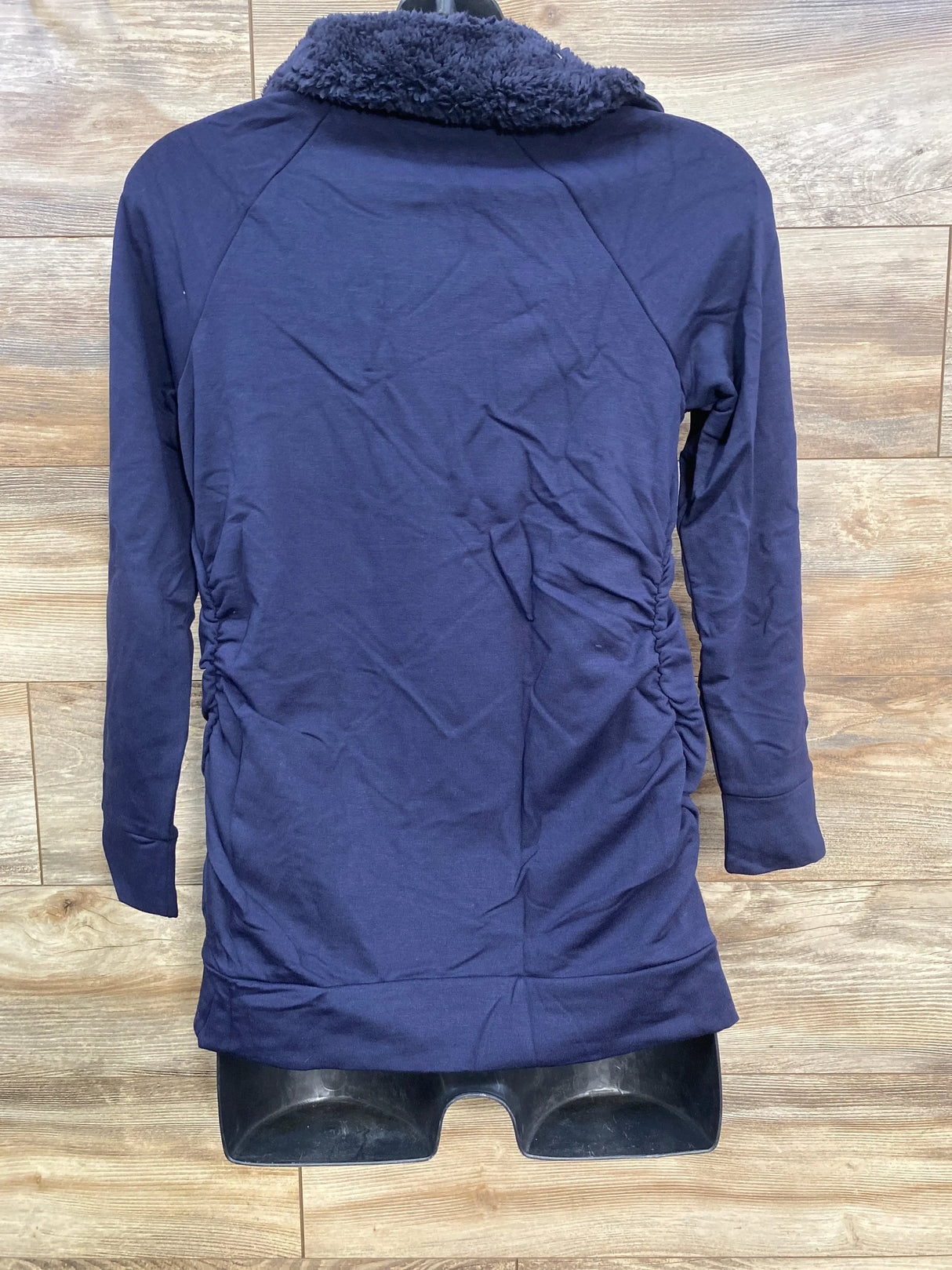 Back view of navy maternity sweatshirt showing sherpa collar and side ruching on wood-plank background