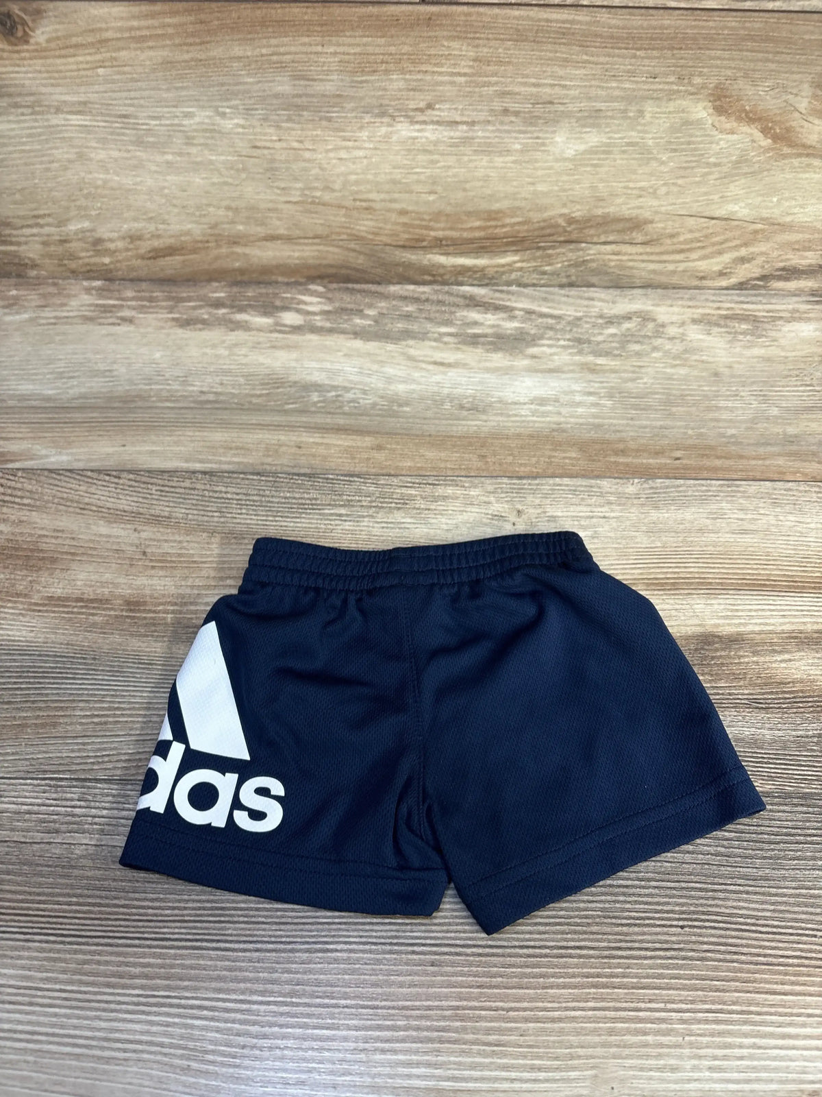 Flat lay of Adidas navy mesh shorts showcasing large white trefoil logo and elastic waistband on wood plank floor