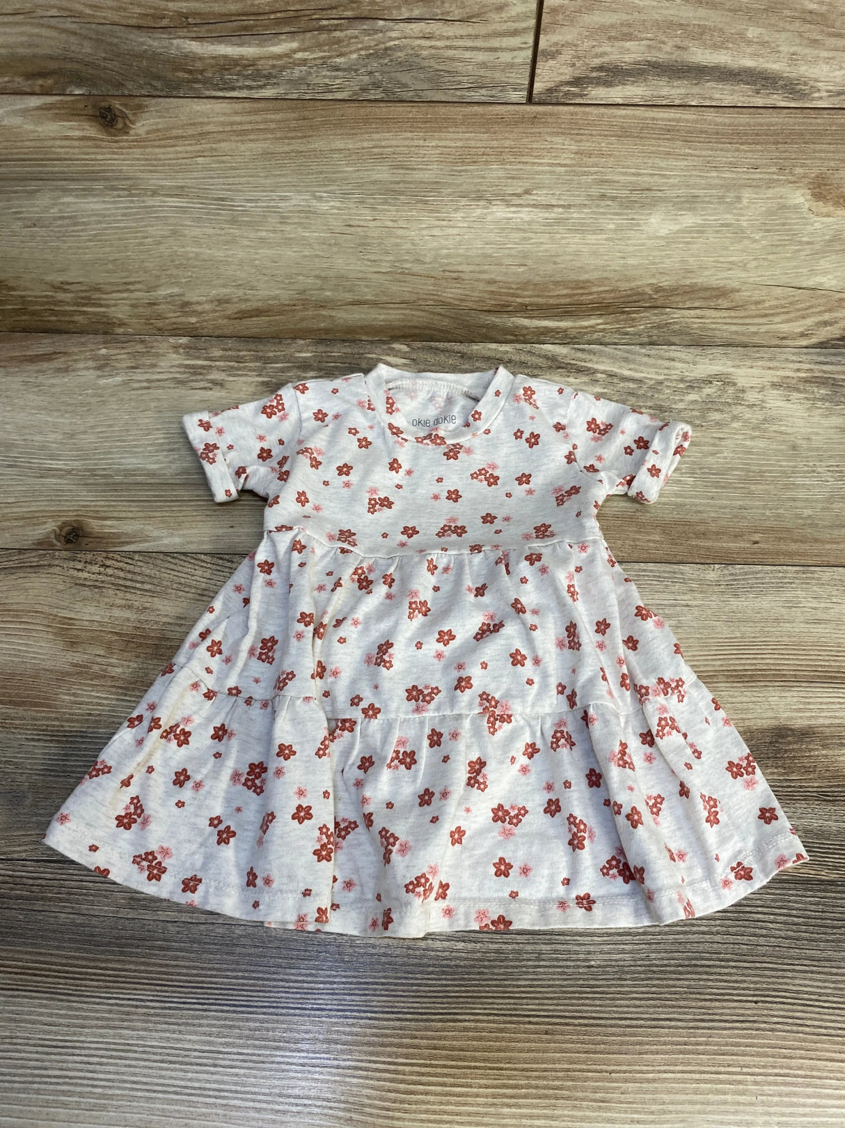 Baby girl's short sleeve floral dress with red flowers on a light background, laid flat on wood