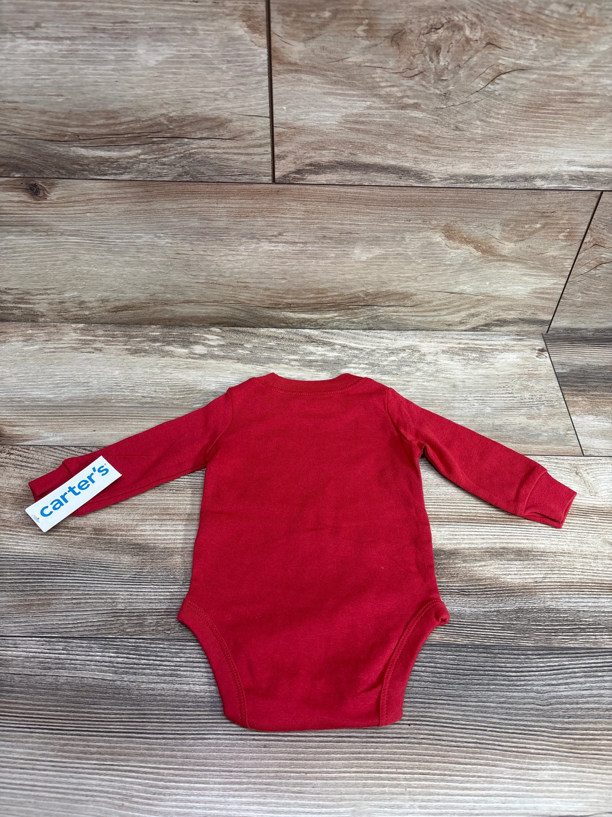 New red long sleeve Carter's baby bodysuit size 3m on a wooden background.