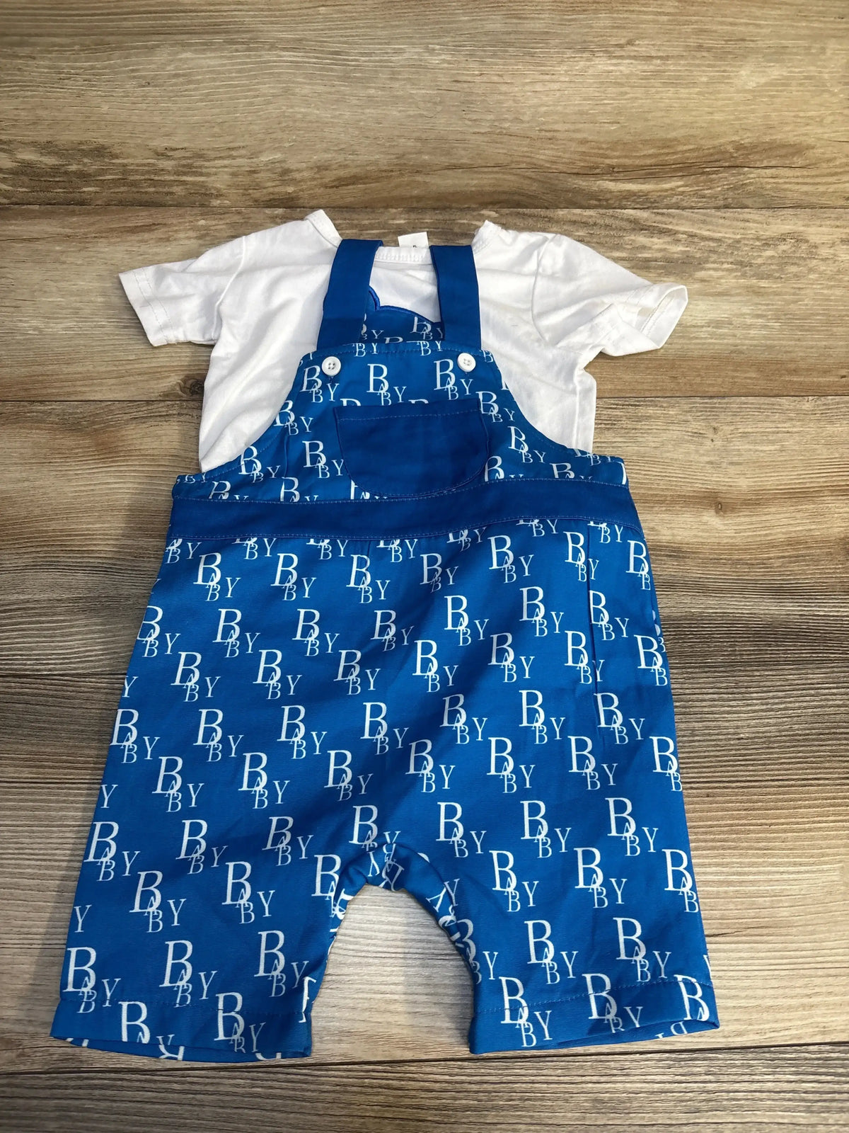 Blue baby overalls with 'BABY' print and white shirt, kids clothing set on wood floor