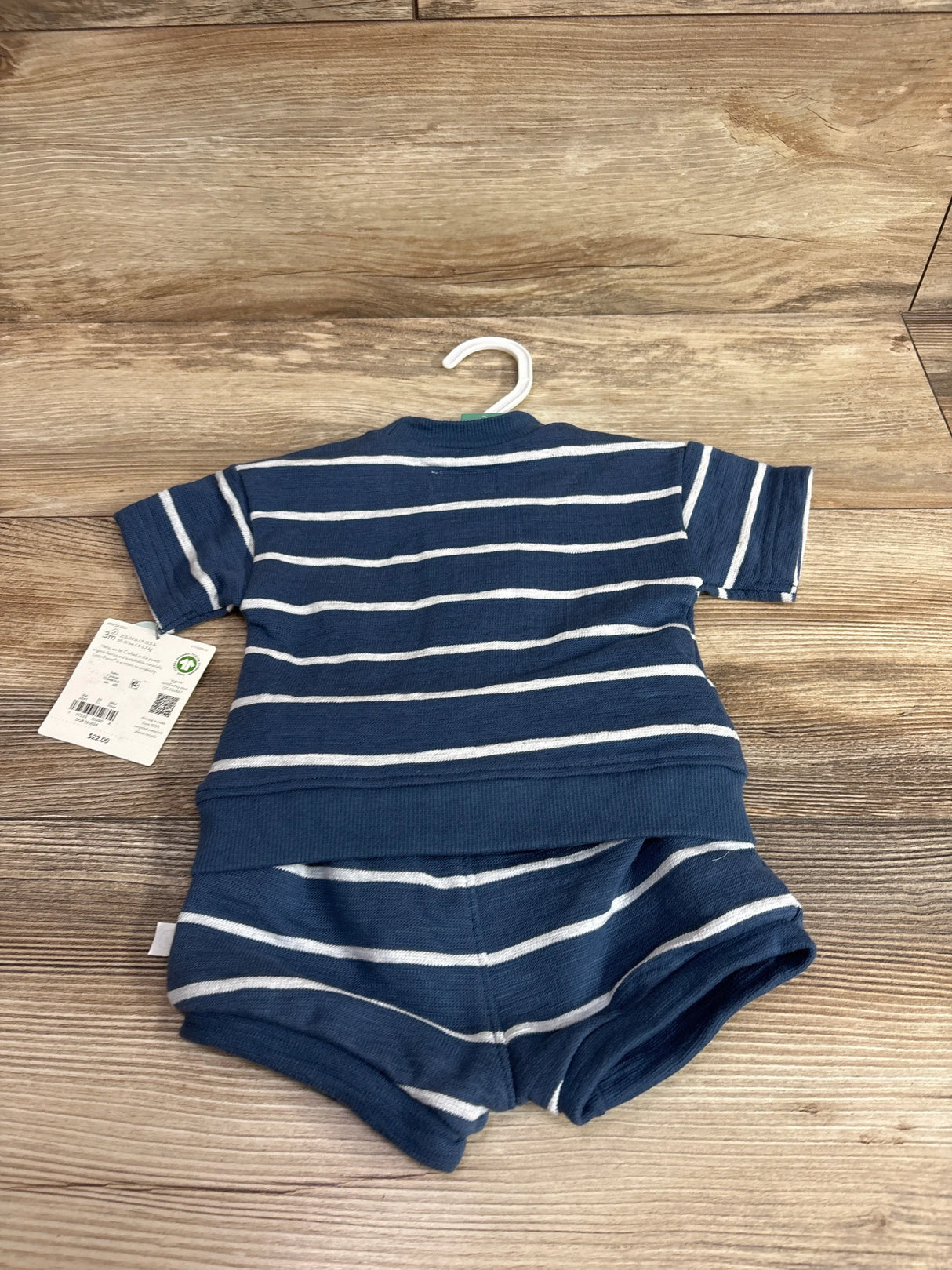Flat-lay of Little Planet organic baby 2-piece set: navy and white striped short-sleeve top and matching shorts on wood floor