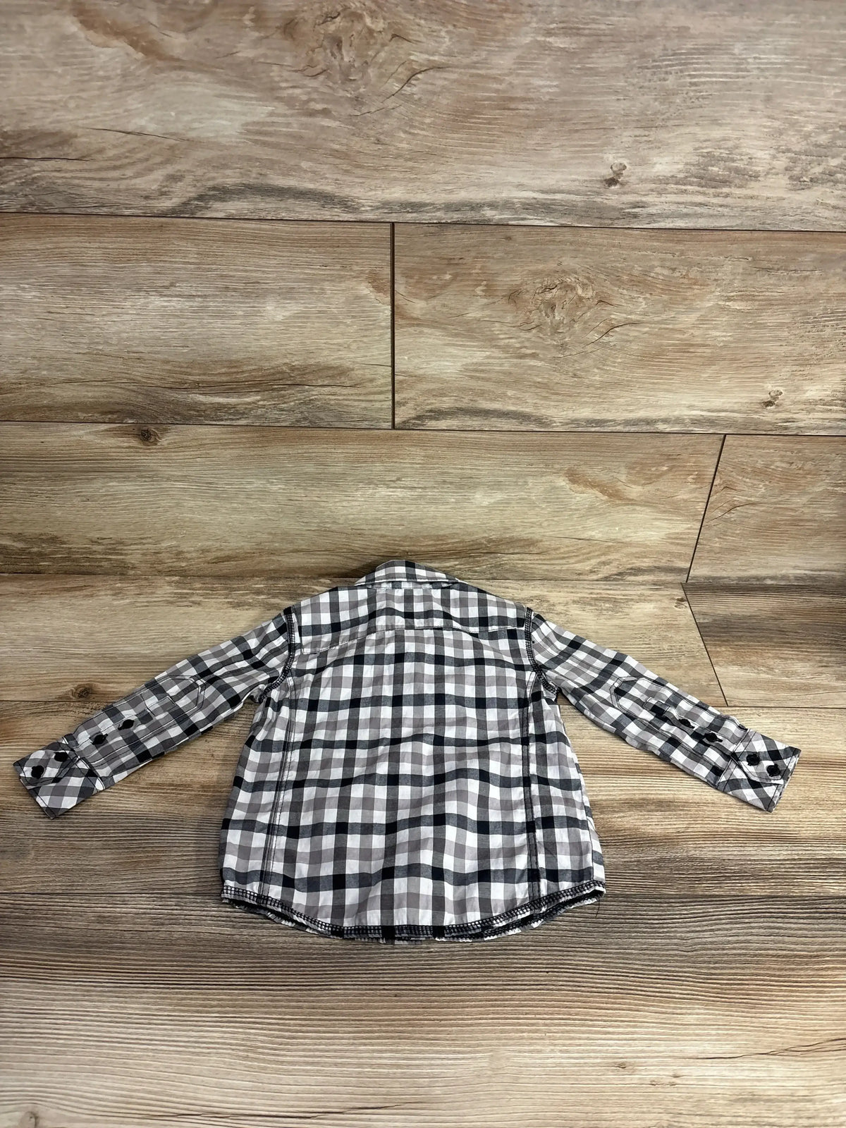 Back view of a black and gray checkered long-sleeve toddler shirt on wood floor