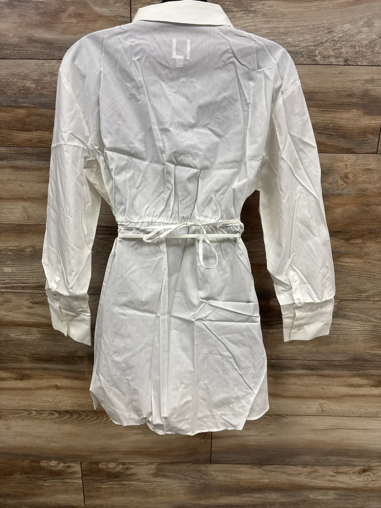White long sleeve collared shirt for children with waist tie, displayed on wood background
