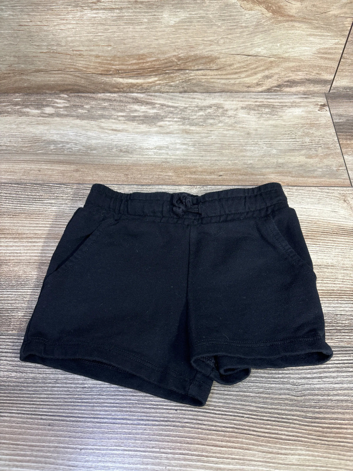 Front view of Cat & Jack black knit shorts in size 2T showcasing drawstring waist and side pockets on a wood-look floor