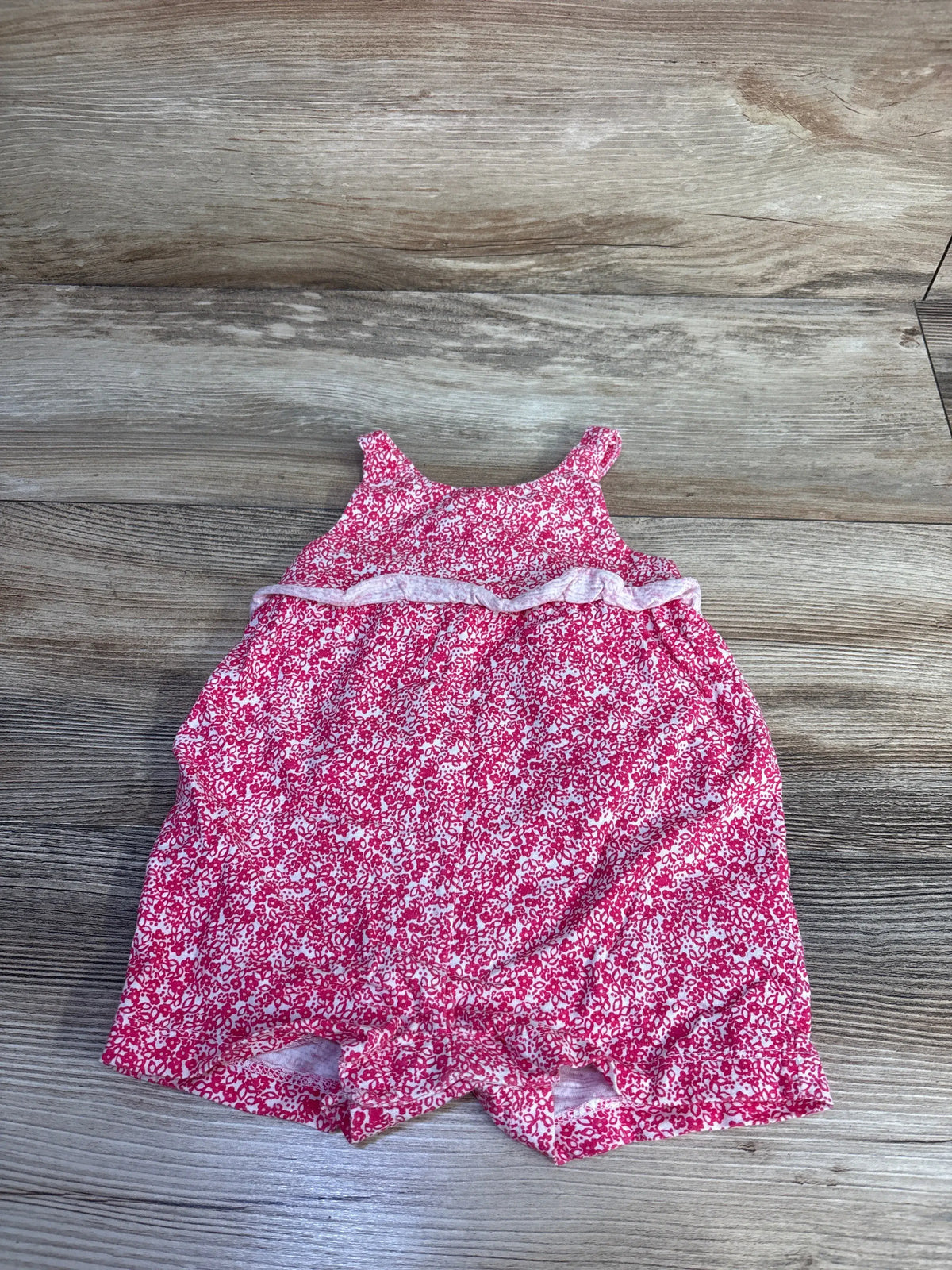 Front view of Carter’s pink shortie romper in size 6 months, with floral print and ruffled trim on wood background