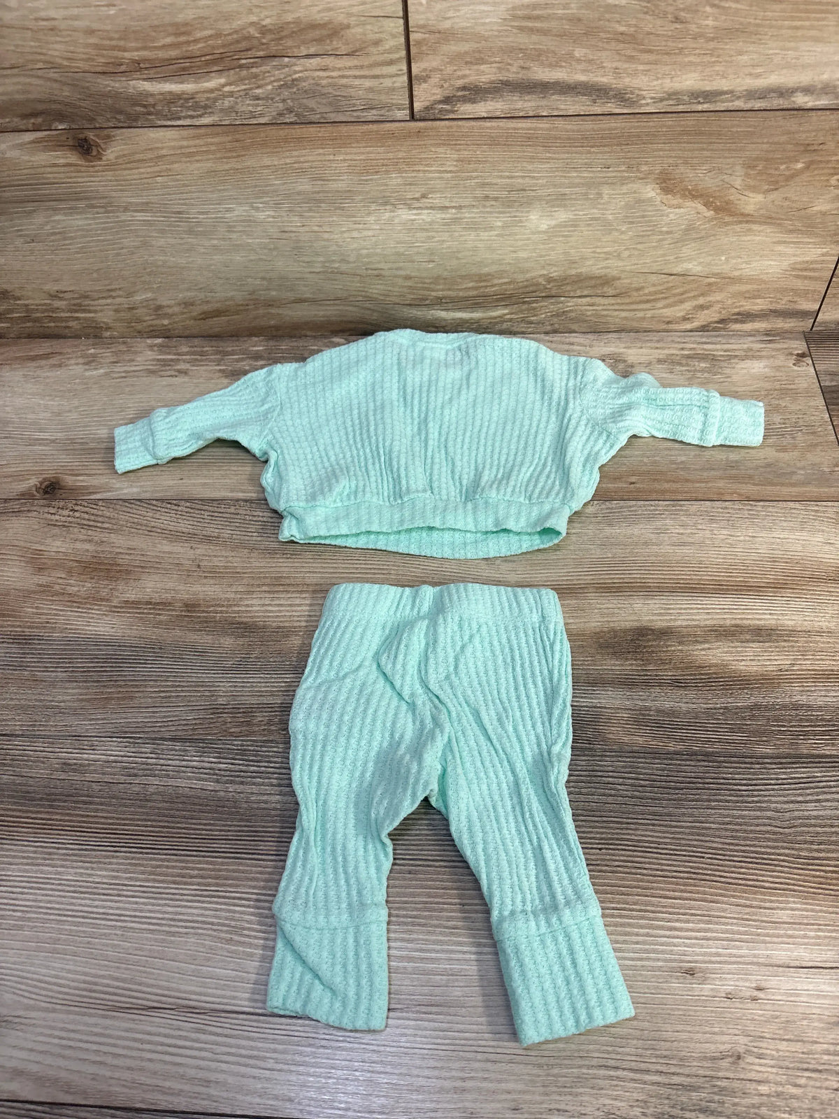 Top-down view of Cat & Jack newborn two-piece set showcasing a textured teal shirt and coordinating pants on a wood surface