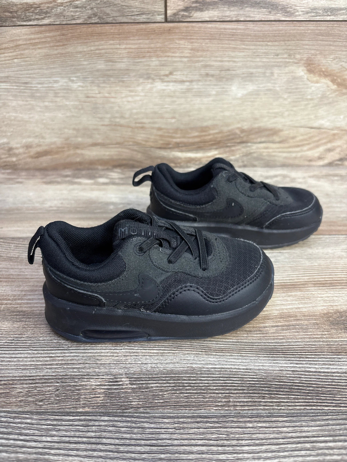 Side view of Nike Air Max Motif PS sneakers size 8C, black with stitched Swoosh and visible Air sole on wood background