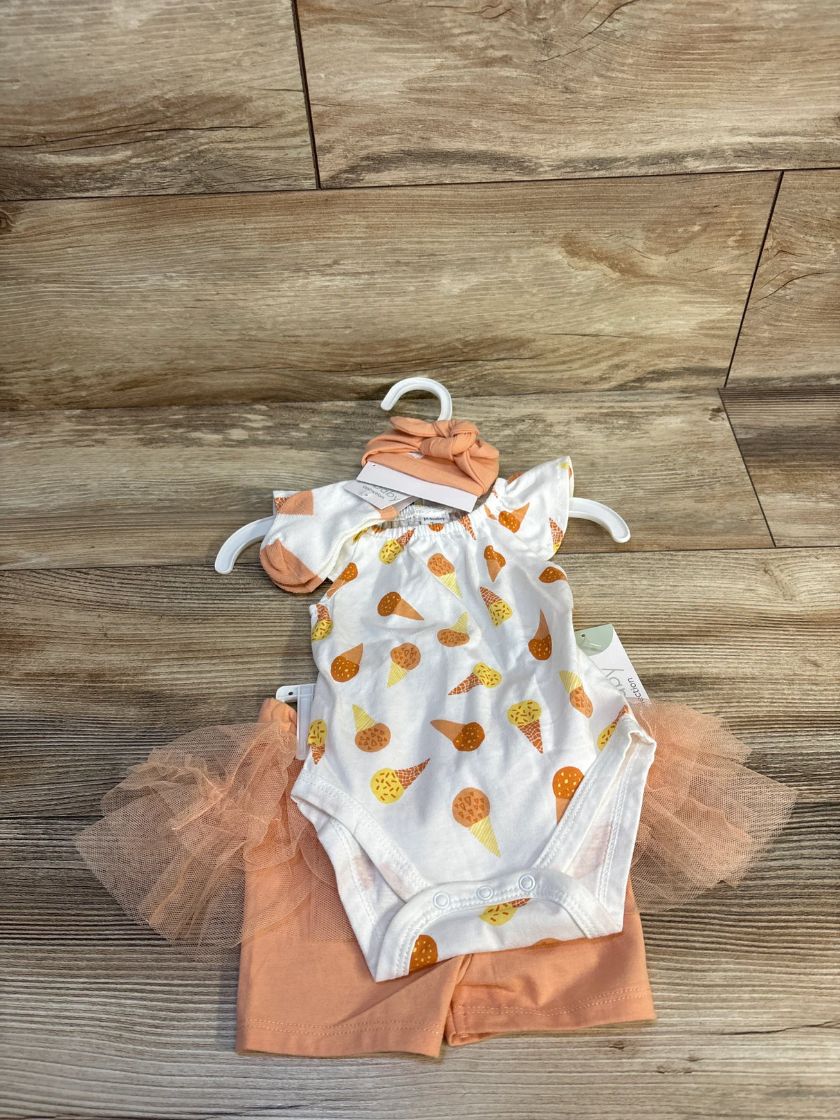 Baby onesie with ice cream print, peach tutu shorts, and matching headband on wood floor
