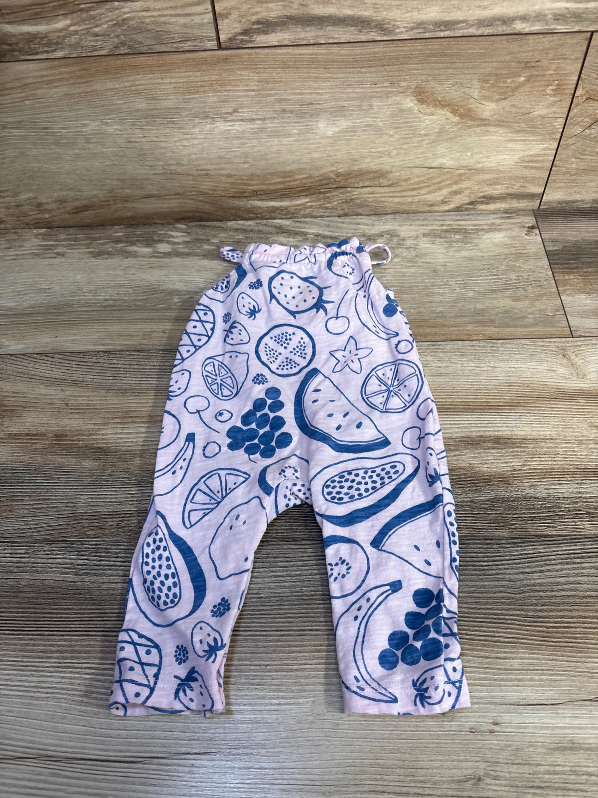 Front view of Cat & Jack pink jumpsuit showcasing a fruit print and sleeveless design on a wood-look floor
