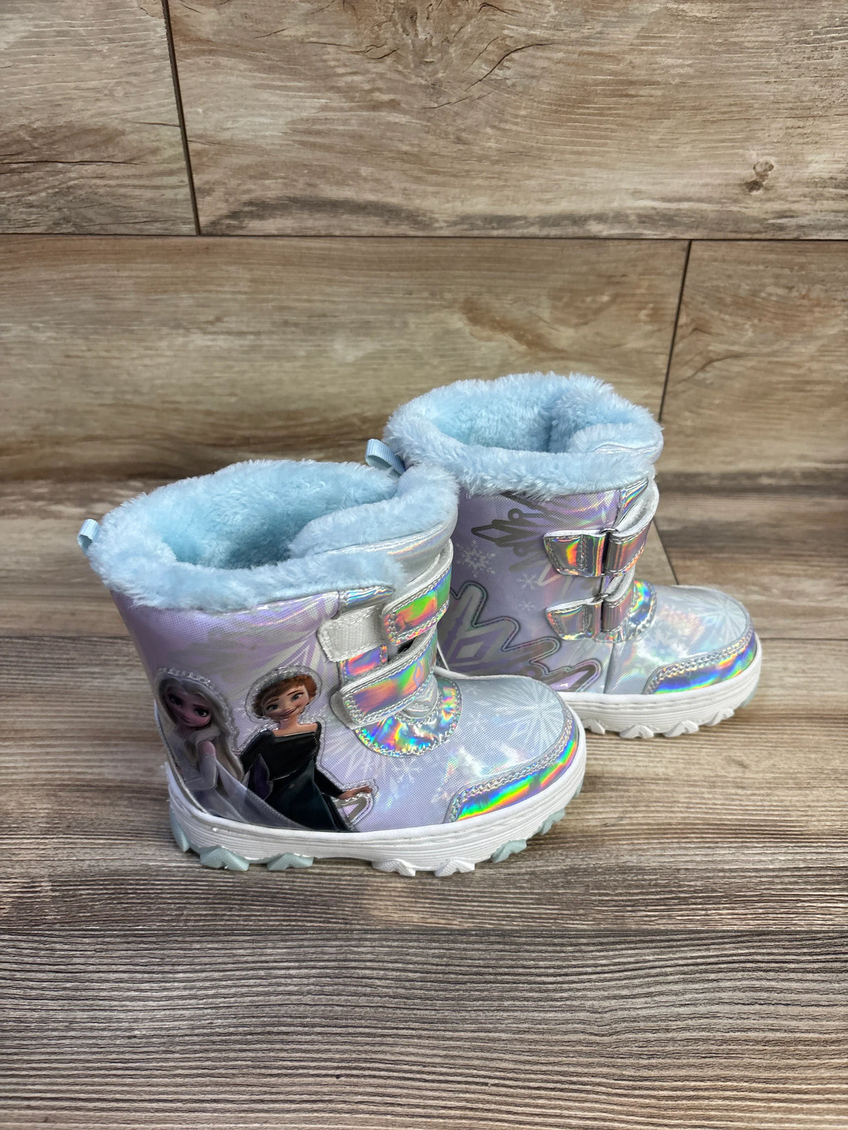 Side view of Disney Frozen snow boots, holographic silver finish, blue faux-fur lining, Velcro straps, on wooden floor