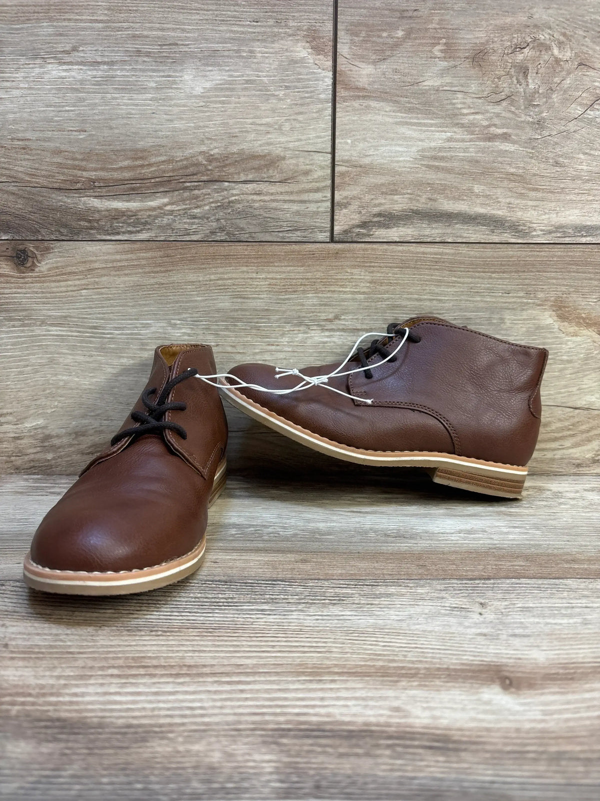 Brown leather kids chukka boots with black laces on wood floor background