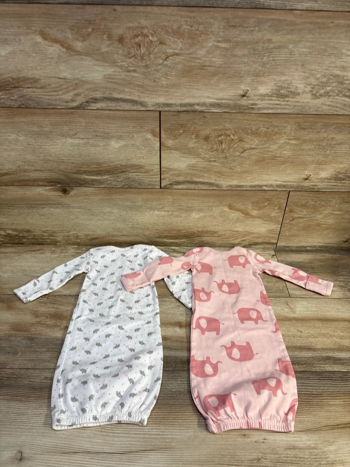 Top view of Simple Joys 2pk sleep gowns showcasing one white animal print gown and one pink elephant print gown on a wood floor