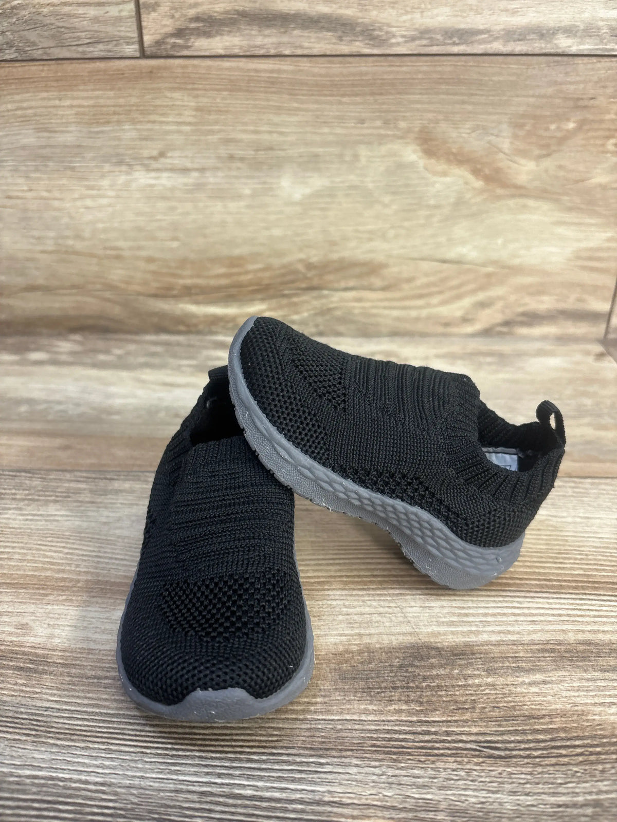 Angled view of Carter’s Taylen pull-on athletic sneakers showcasing black knit uppers and gray soles on wood