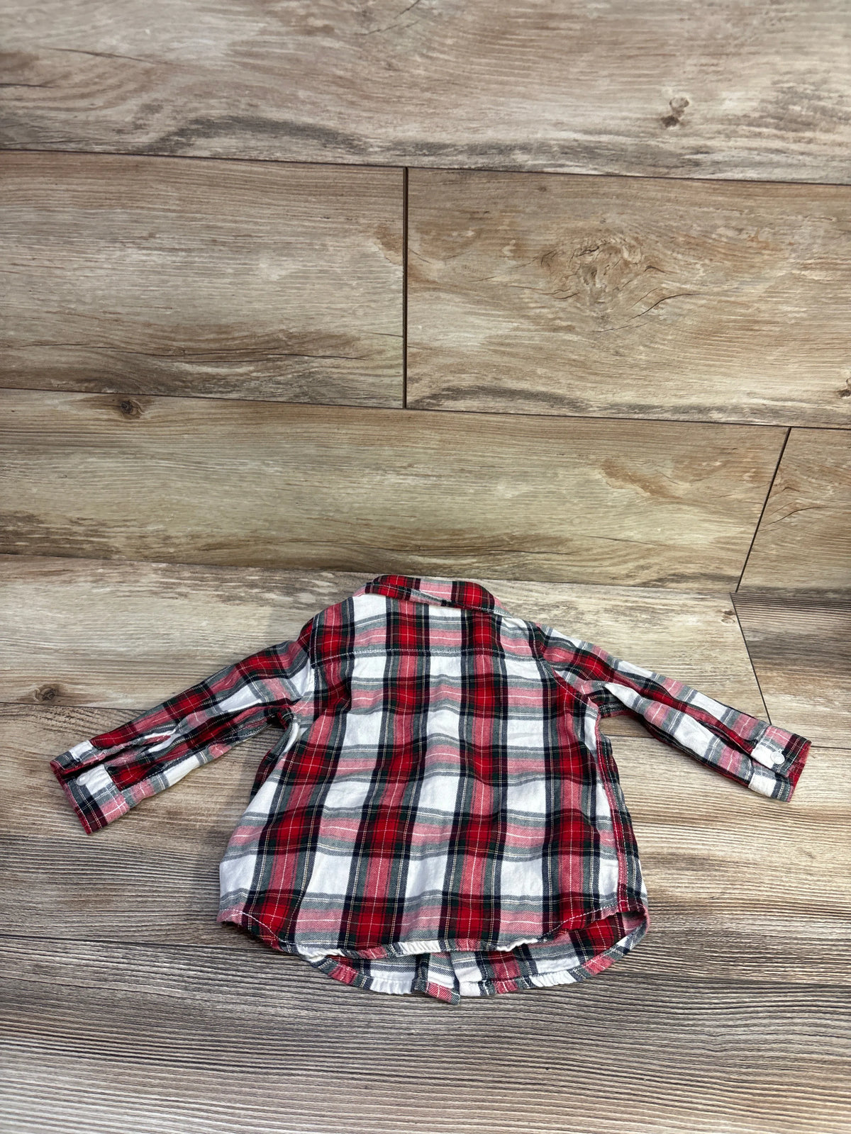 Flat lay of H&M red plaid button-up flannel shirt in size 6 months showcasing long sleeves with a wood background