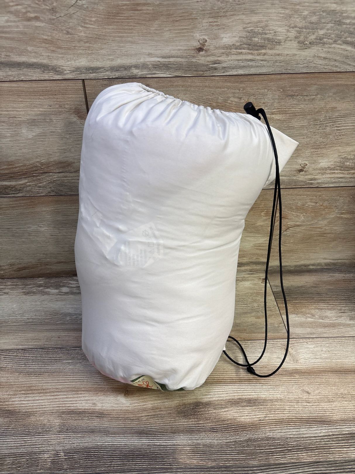 Front view of Firefly! Sparkle the Unicorn Kid’s sleeping bag rolled in white drawstring sack on wood background