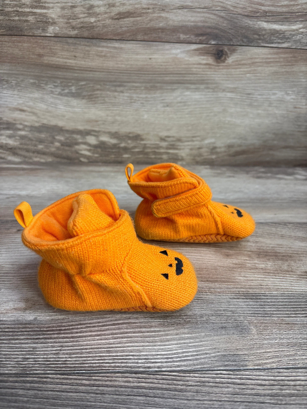 Orange baby booties with cute jack-o'-lantern faces on wooden surface