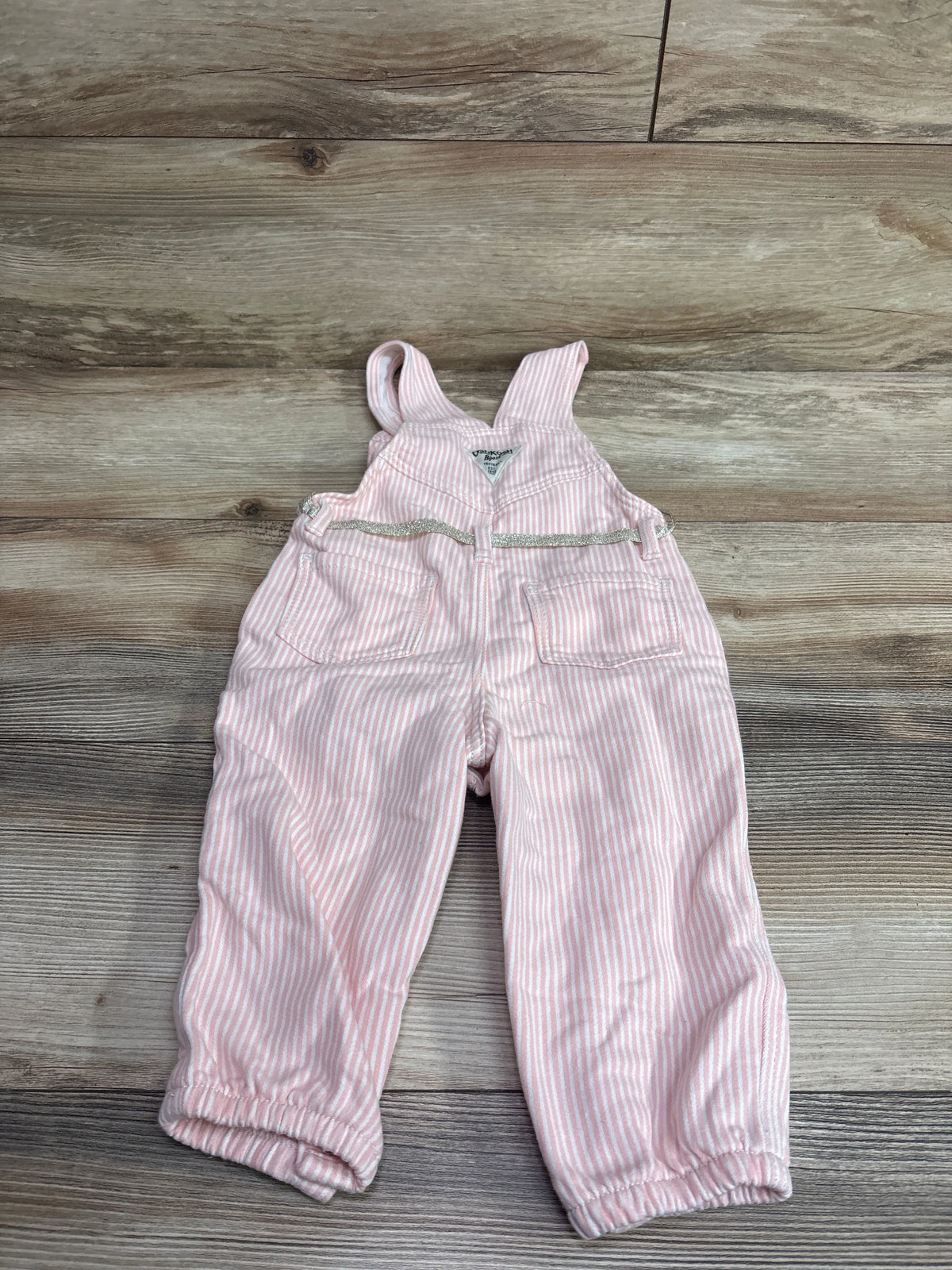 Pink and white striped baby overalls by Me n Mommy To Be on a wooden surface.