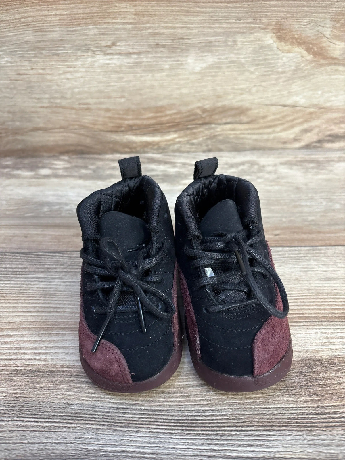 Black and burgundy suede baby sneakers with laces on wood background