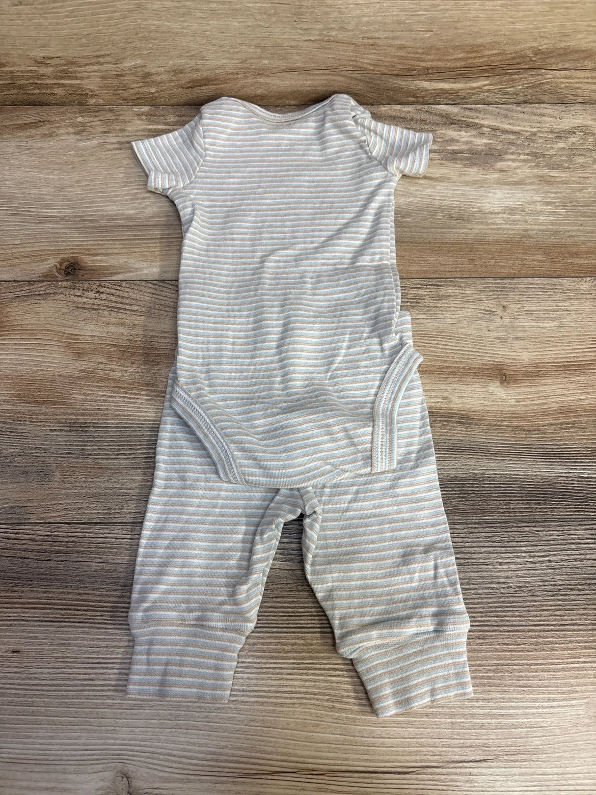 Flat lay of striped short-sleeve bodysuit and matching pants in cream with thin beige and blue stripes on wood background
