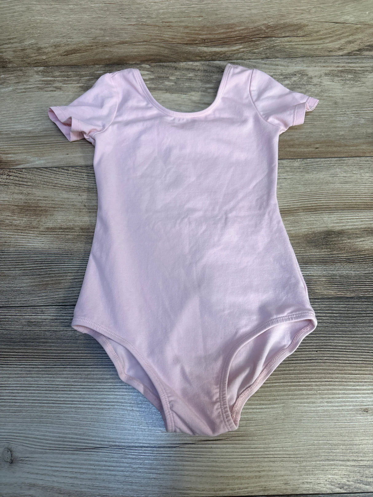 Light pink short sleeve toddler leotard on wood background