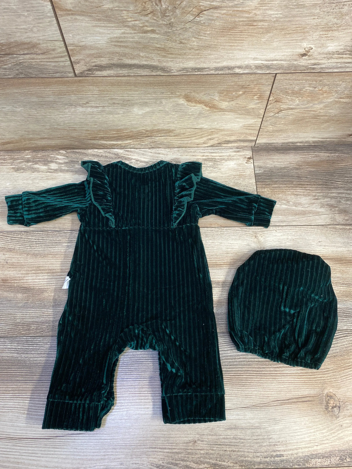 Green velvet baby romper and matching hat on wooden floor
