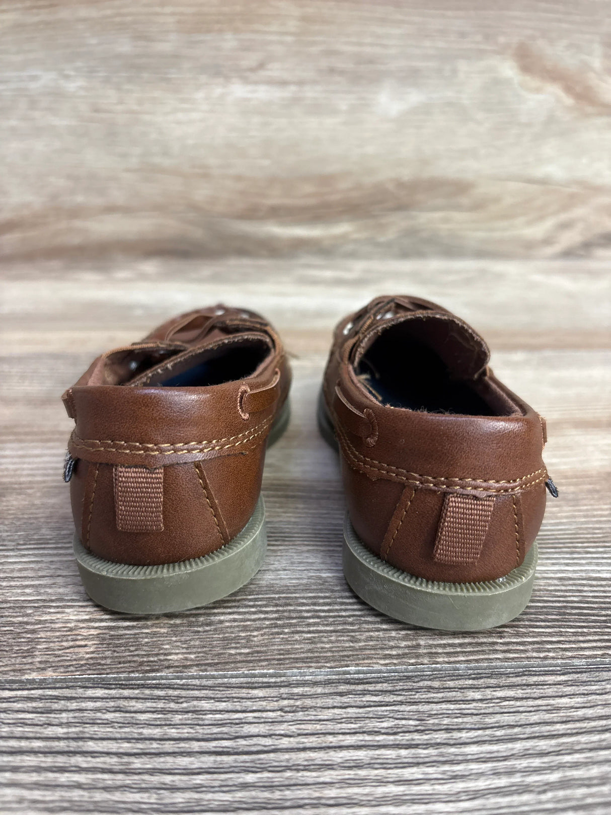 Pair of brown children's leather boat shoes with gray soles on wooden floor