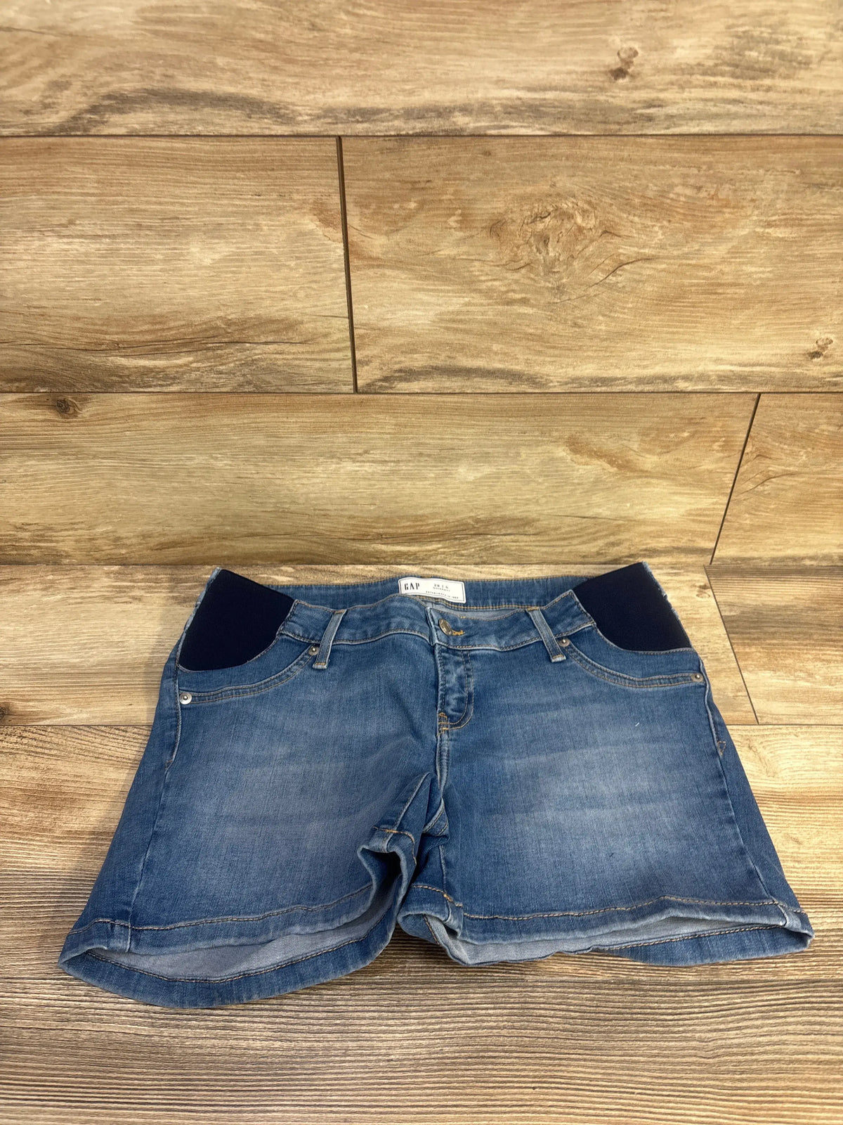 Front view of Gap maternity denim shorts in medium wash blue showcasing four inch inset panels with a wood floor background