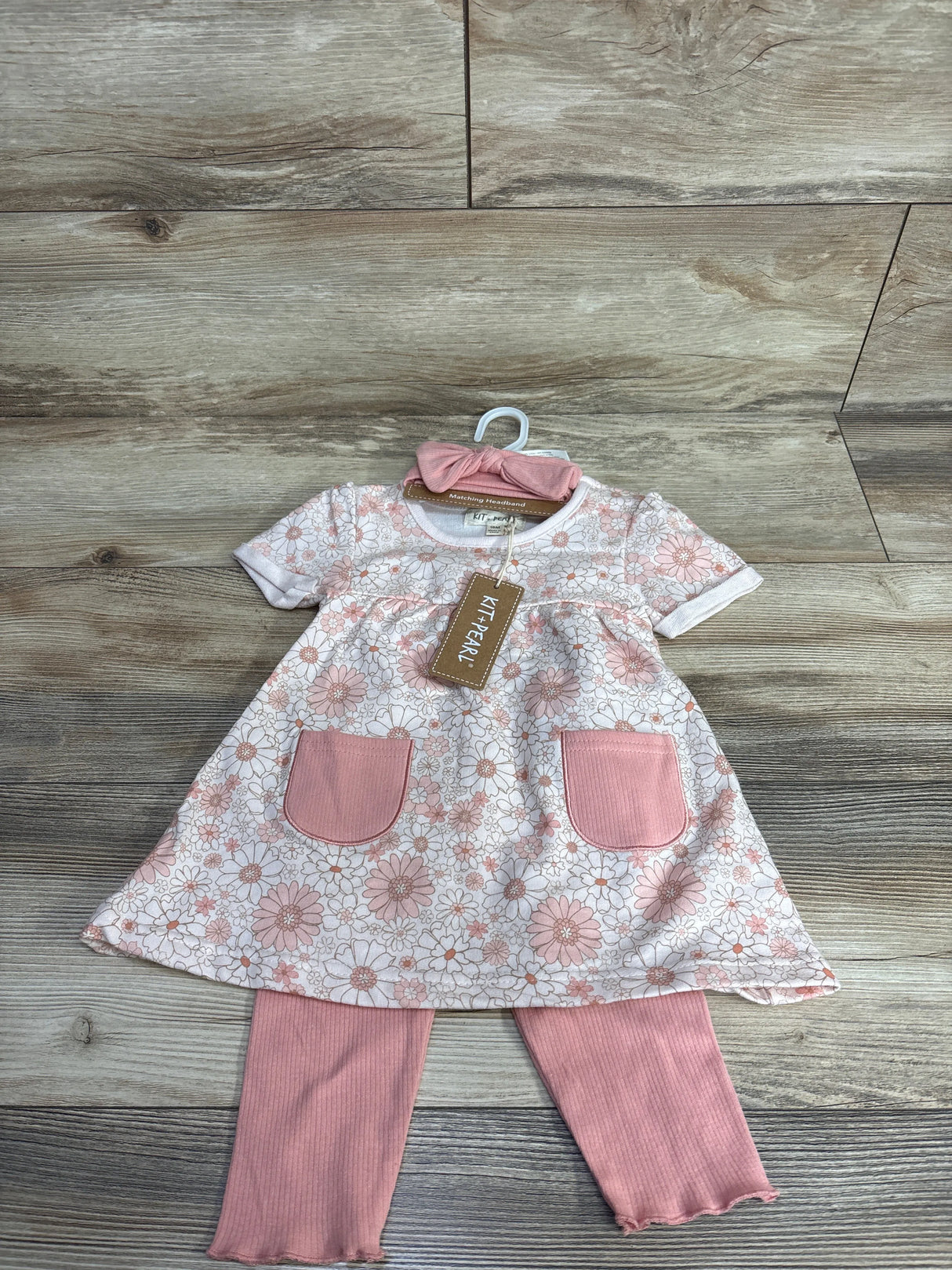 Floral baby dress with pink pockets, matching pink leggings, and headband on wooden floor