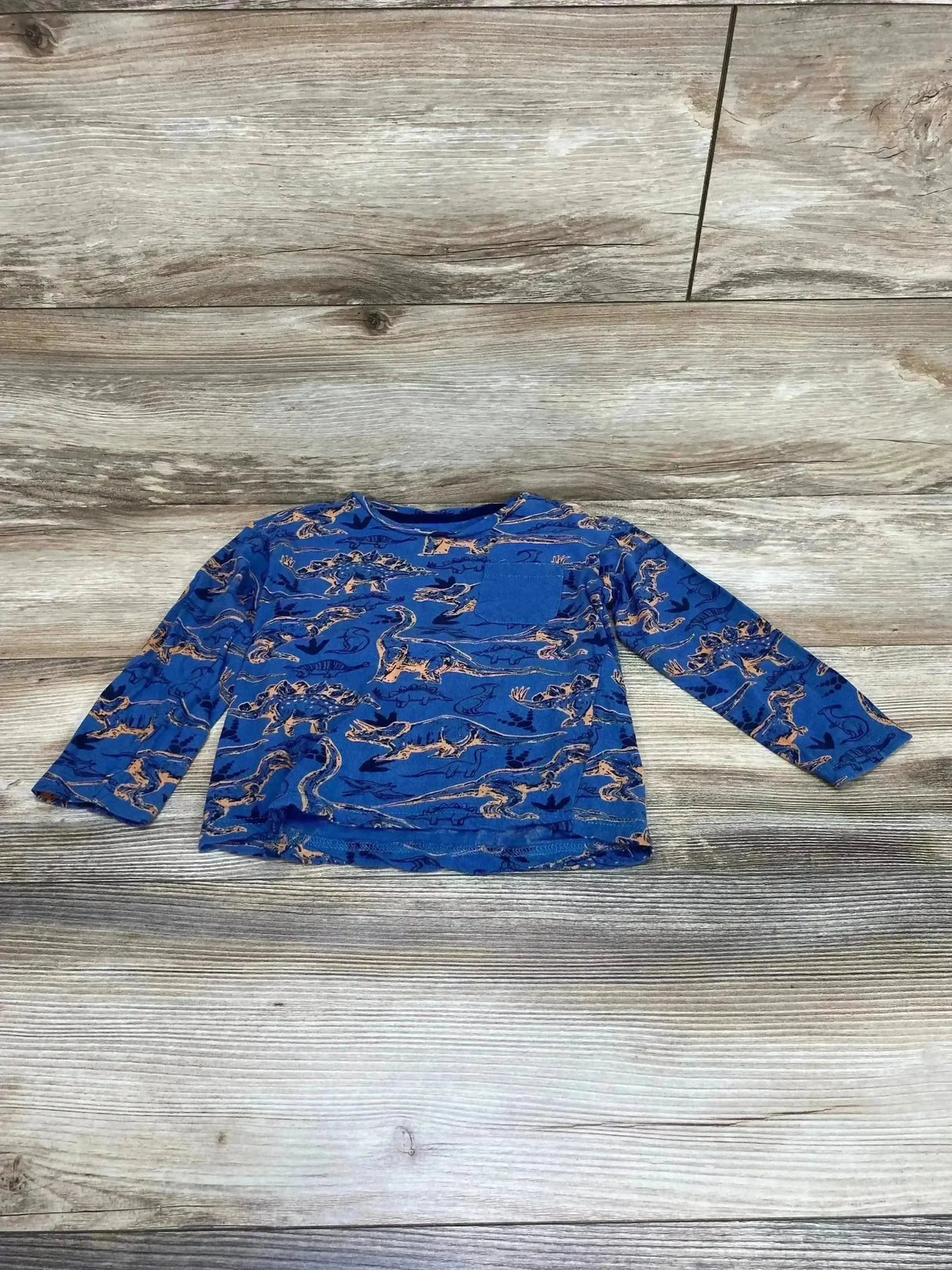 Flat lay of toddler long-sleeve blue dino shirt size 4T with orange dinosaur print and chest pocket on wood background