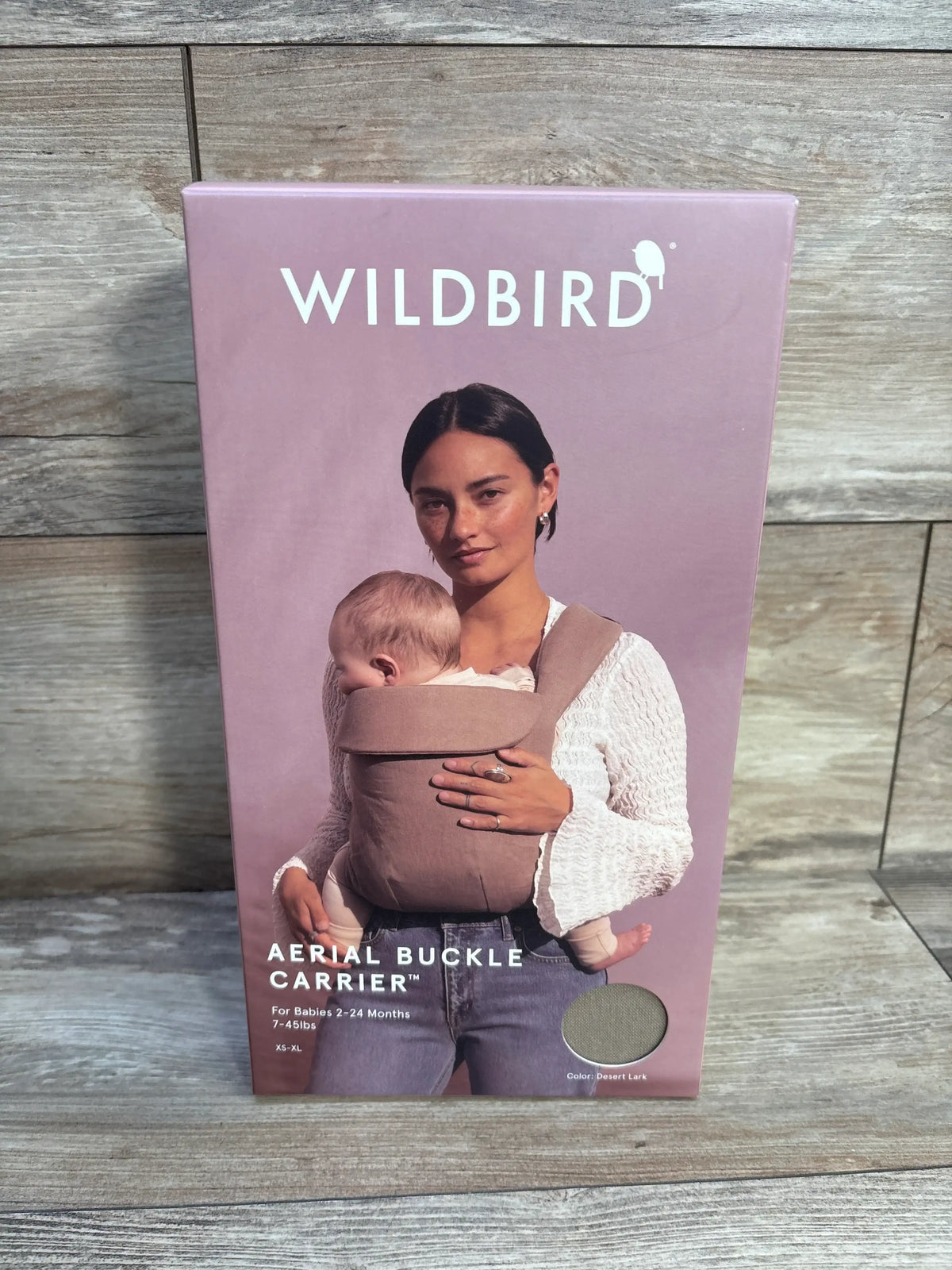 Front view of WildBird Aerial Buckle Carrier in Desert Lark, shown on packaging with a baby worn inward