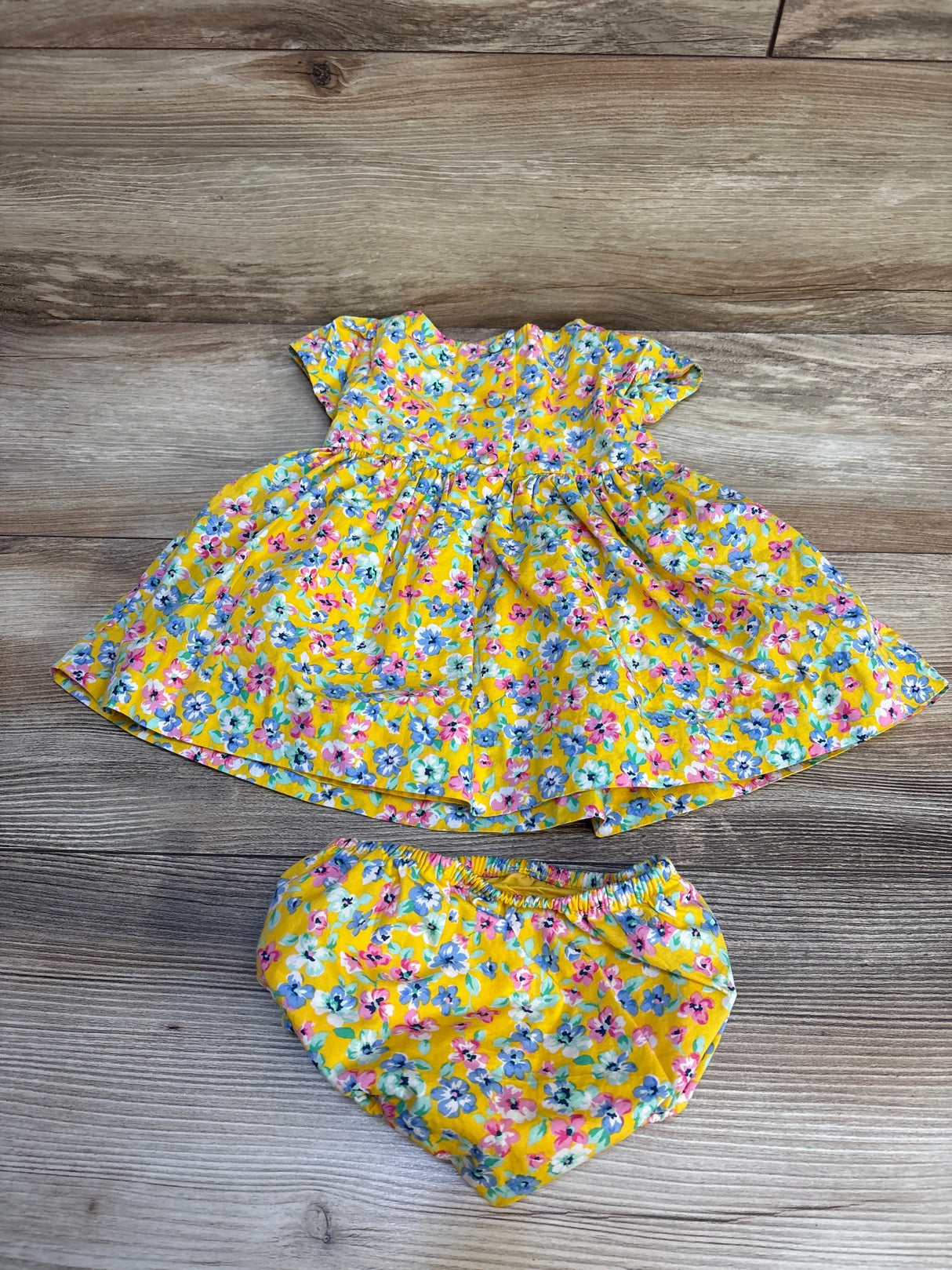 Yellow floral baby dress with matching bloomers on wood background