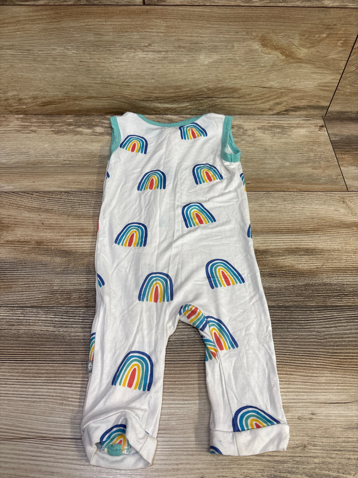 Front view of the Kyte Baby white sleeveless zipper jumpsuit with rainbow pattern, laid flat on a wood surface
