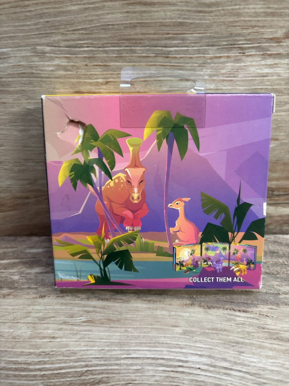 Front view of Make-It Blocks Dino Construction Playset box showing colorful cartoon dinosaurs, palm trees, and Collect Them All text on wood background