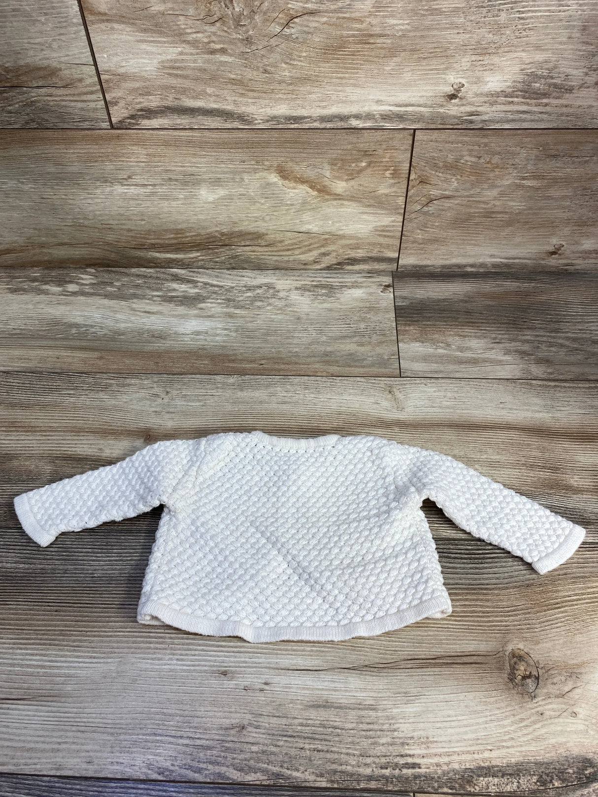 White textured knit baby sweater with long sleeves on wood background