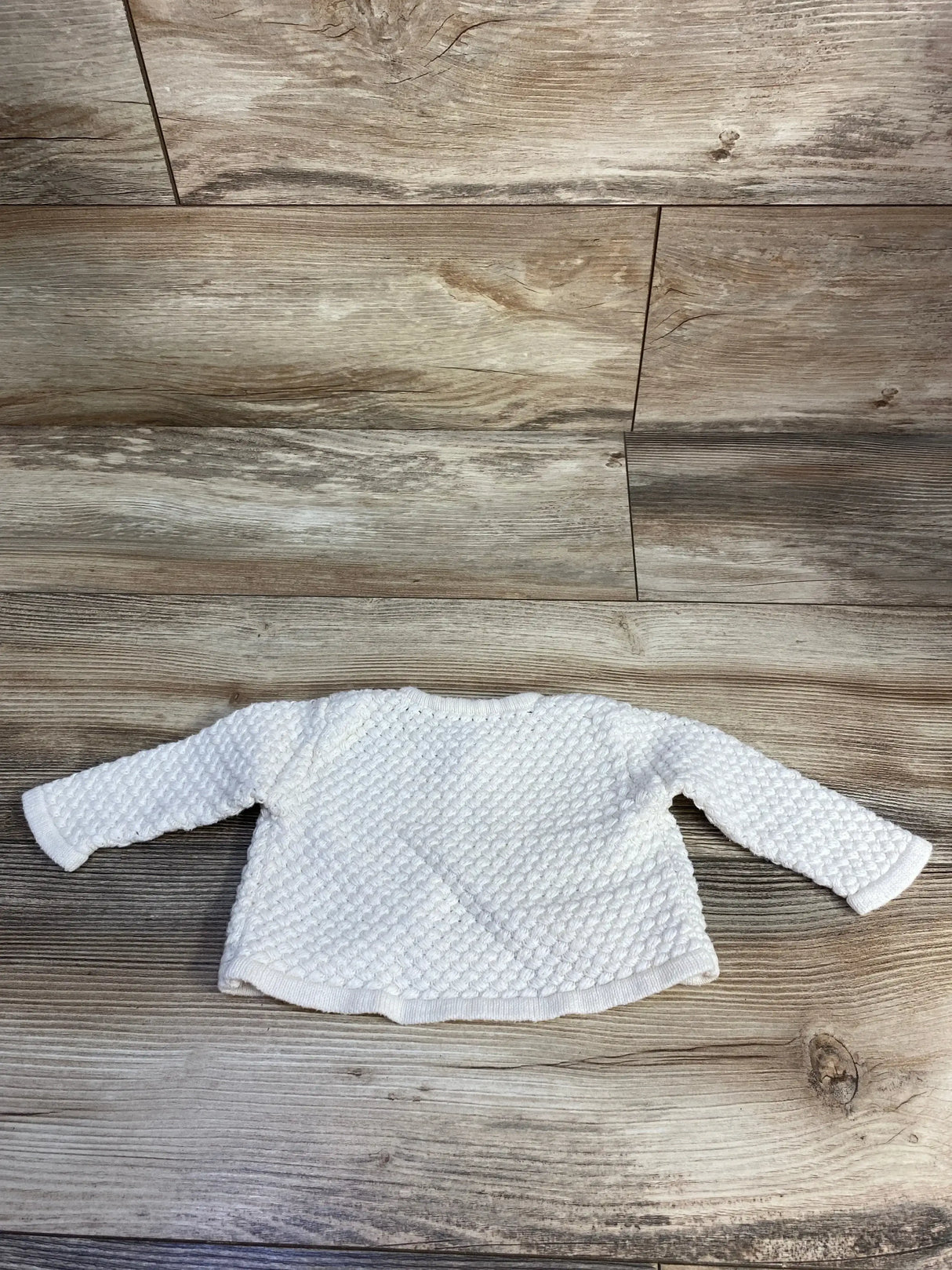 White textured knit baby sweater with long sleeves on wood background