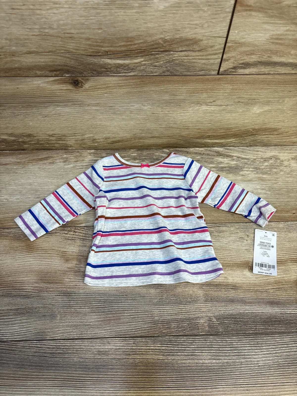 Long sleeve toddler shirt with multicolor stripes and price tag on wood background