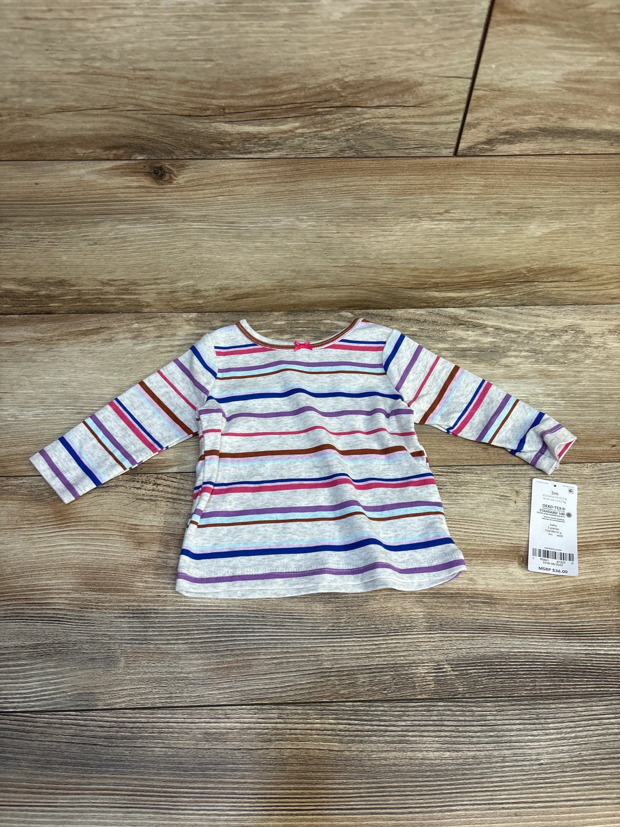Long sleeve toddler shirt with multicolor stripes and price tag on wood background